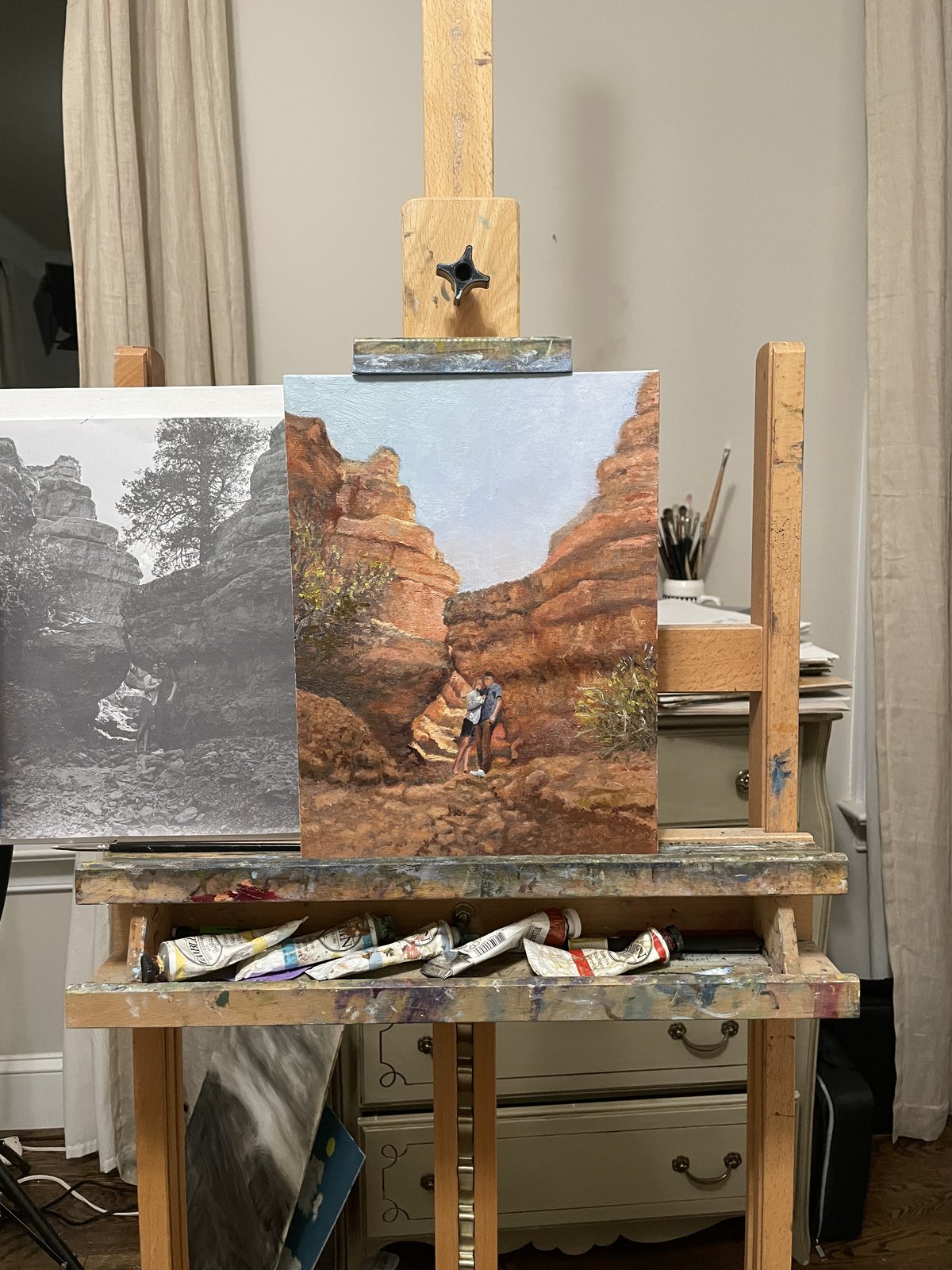 A canvas on the easel beside its reference photograph